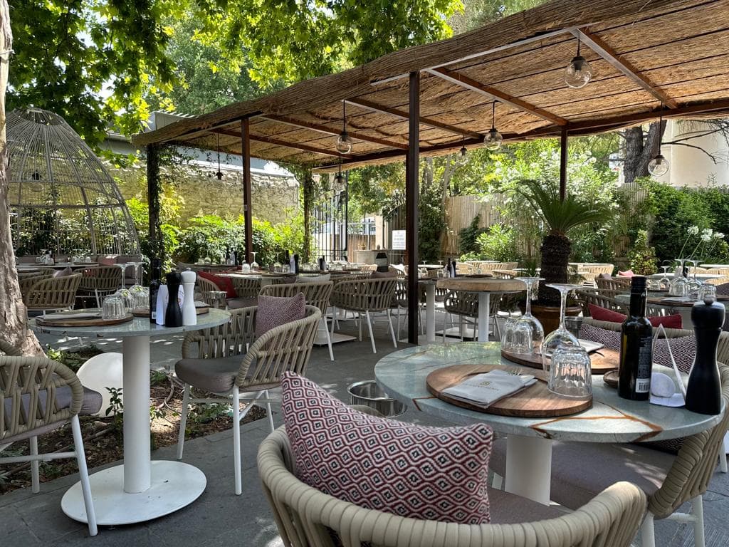 Terrasse de restaurant ombragée, tables dressées, ambiance verdoyante.
